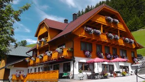 A traditional wooden building with balconies adorned with flowers, a red-tiled roof, and outdoor seating.