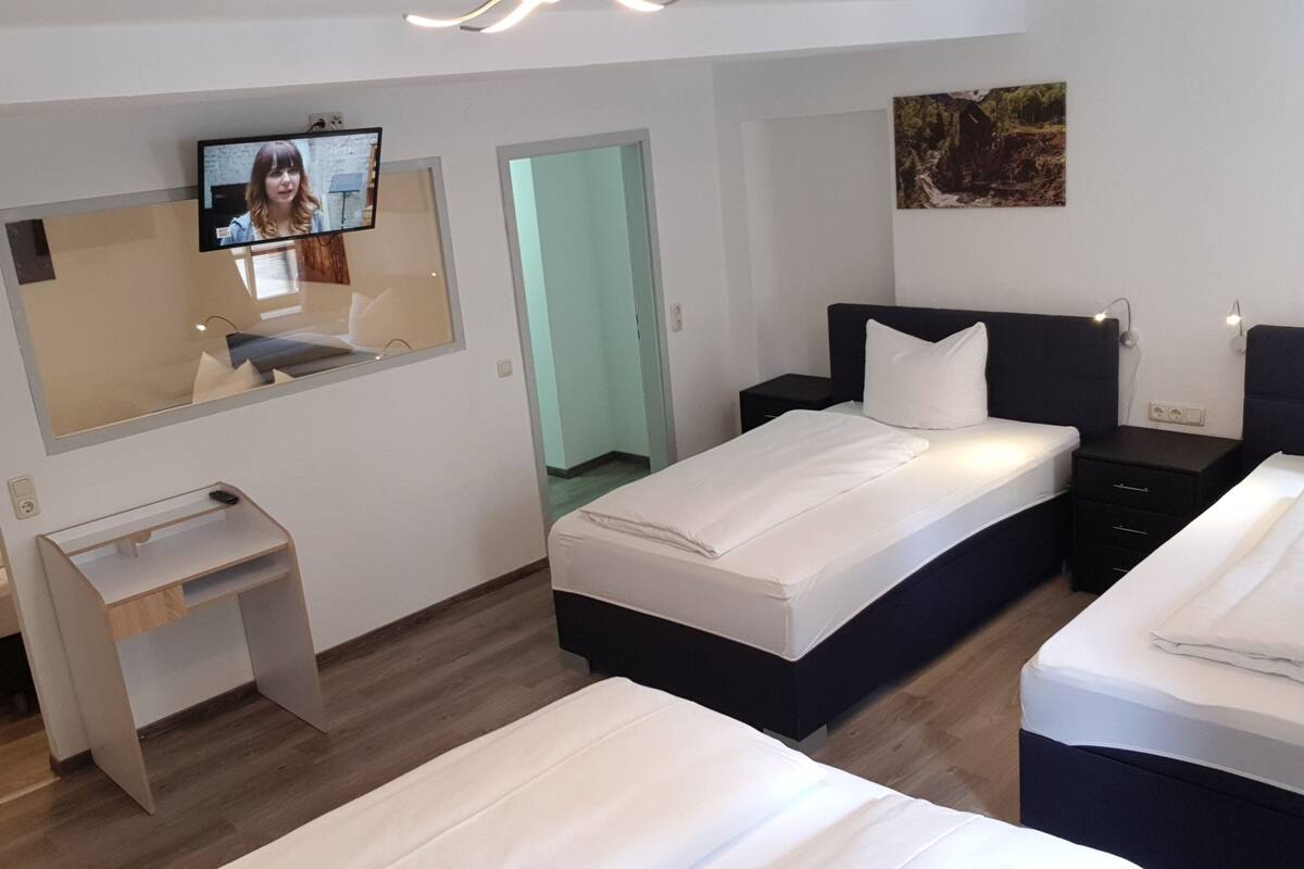A modern hotel room with a bed, a desk, a TV, and a painting on the wall.