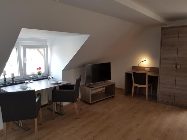 Un dormitorio tipo loft moderno con techo inclinado, un comedor con mesa y sillas, un televisor y un armario.