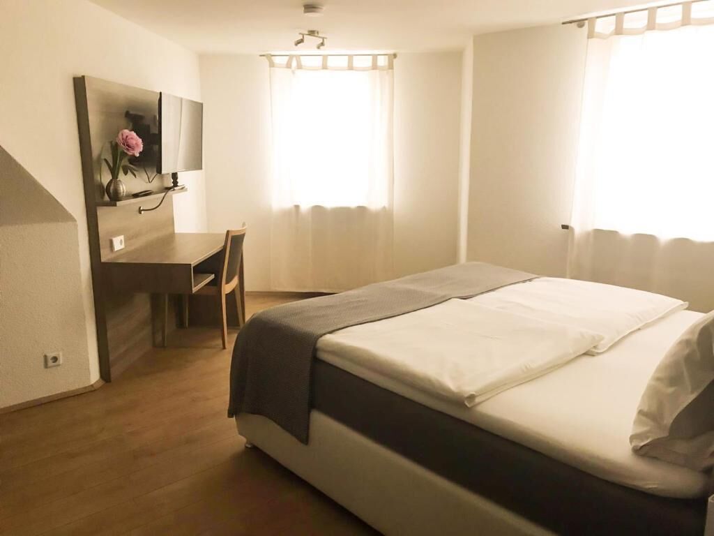 Un dormitorio con cama, escritorio, silla, televisor y ventana con cortinas.