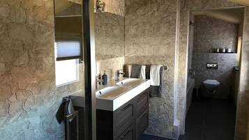 Un baño con paredes de piedra, tocador doble, espejo y retrete.