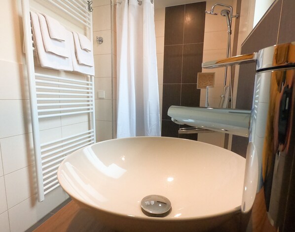 Un baño con un lavamanos blanco, ducha y un perchero para toallas.
