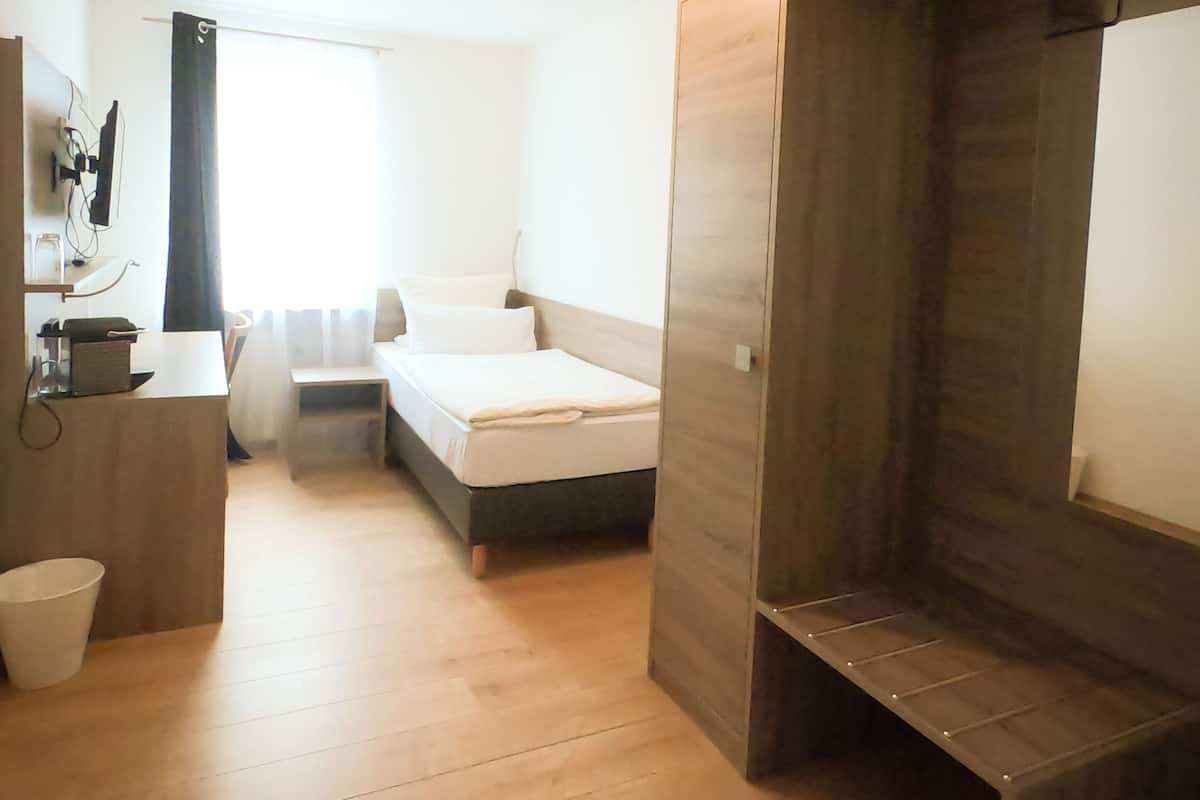 Ein Zimmer mit einem Bett, einem Schreibtisch, einem Stuhl, einem Holzschrank und einem Fenster.