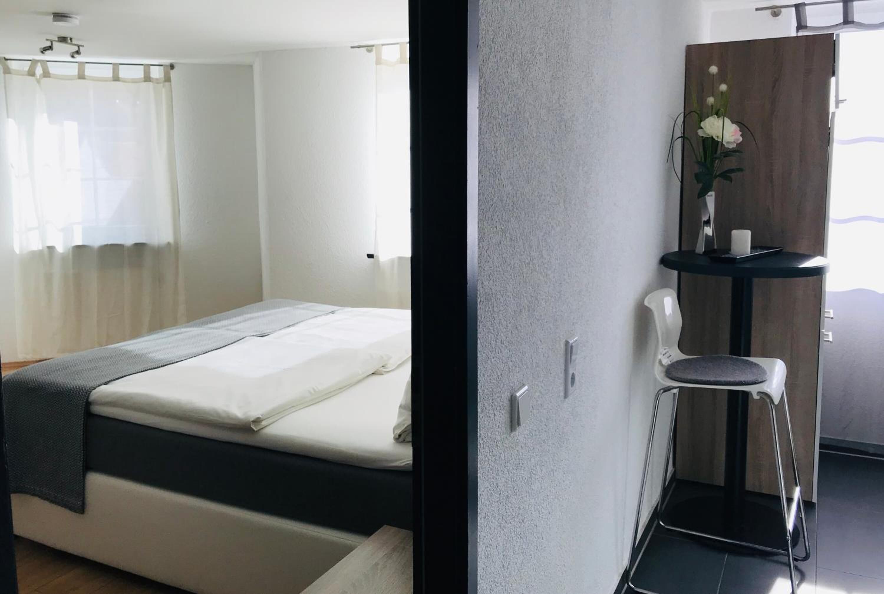 Een slaapkamer met een bed, nachtkastje, stoel, spiegel en raam met gordijnen.