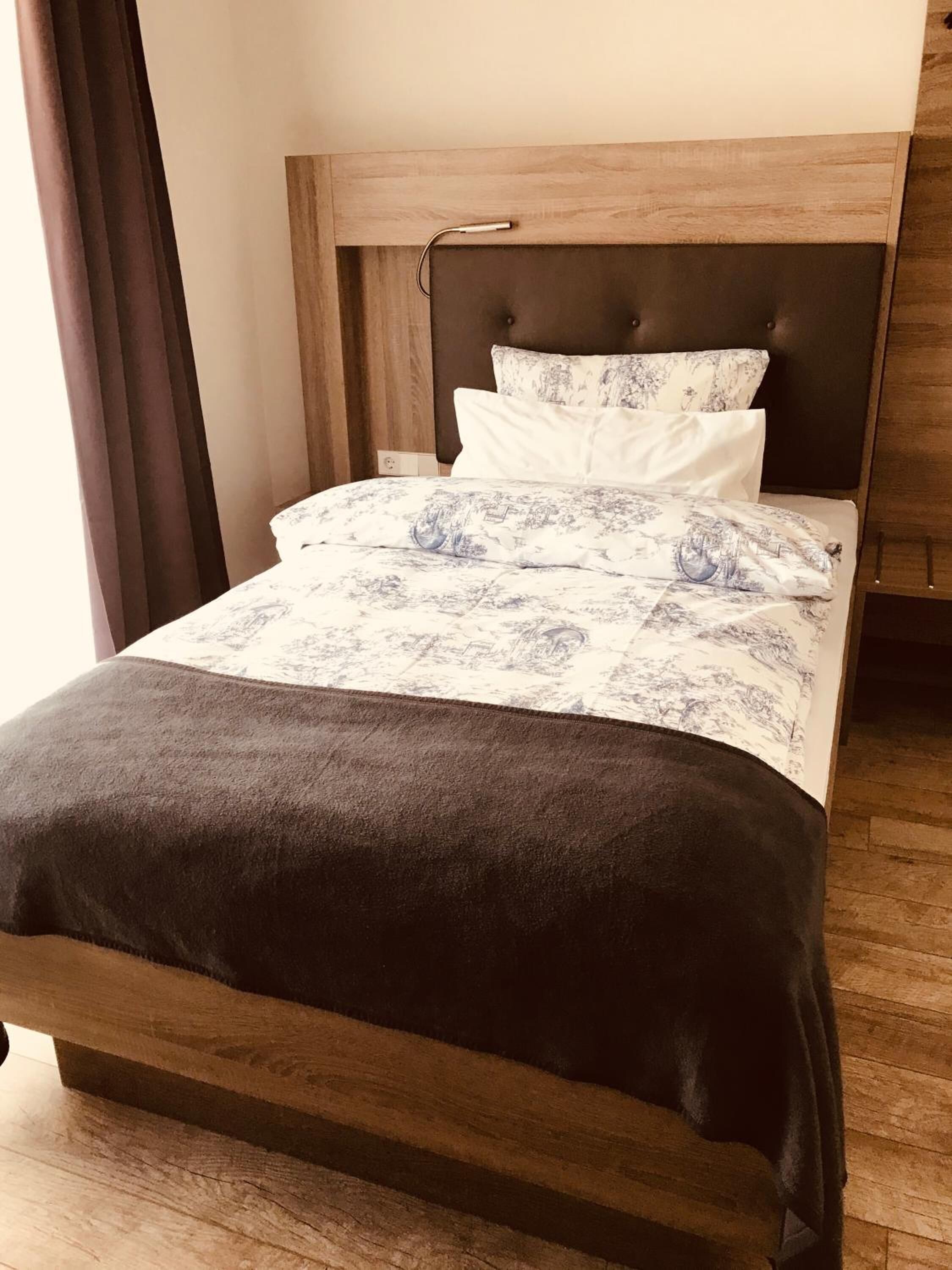 A neatly made bed with a dark headboard, white and patterned bedding, and a wooden floor.