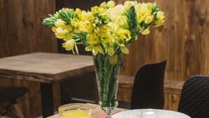 A dining table with a vase of yellow flowers, two glasses of orange juice, a white teapot, and a red napkin. - Potemkinn Hotel (Odesa)