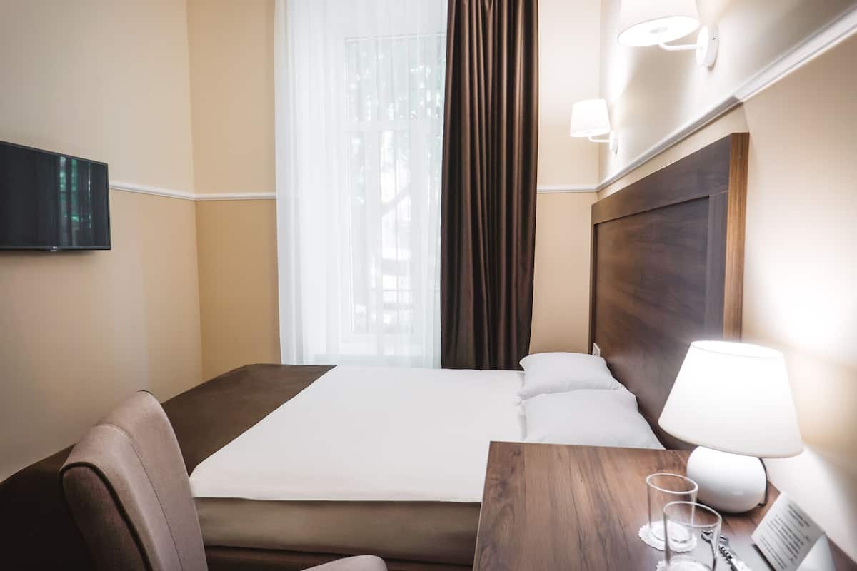A hotel room with a bed, a desk with a lamp, a chair, and a TV mounted on the wall.
