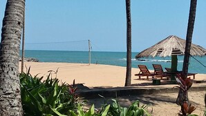 Una spiaggia con una rete da pallavolo, palme e una struttura con tetto di paglia e sedie.