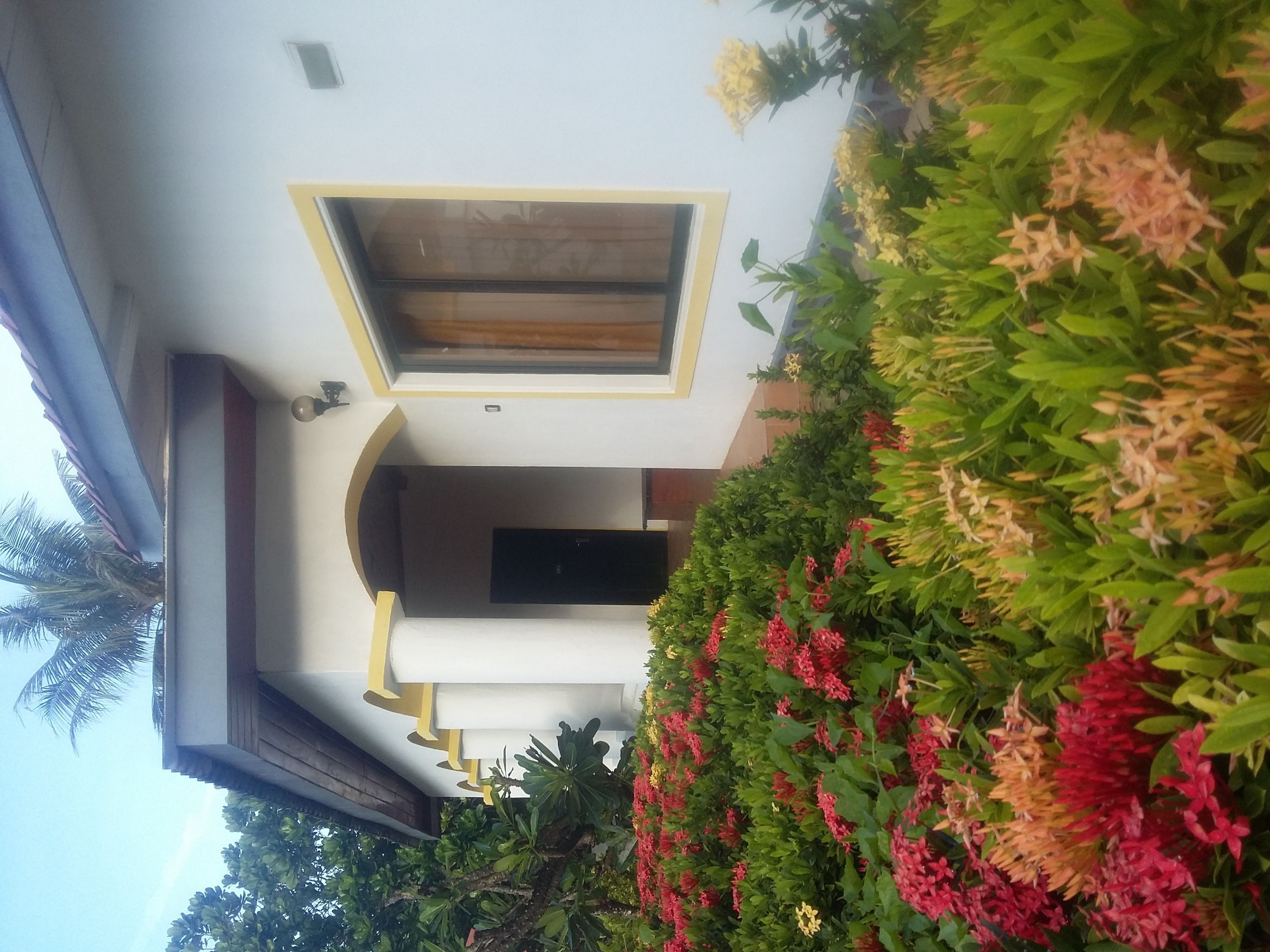Ein modernes Gebäude mit einem zentralen Eingang, einem kleinen Balkon und einem Garten mit bunten Blumen.