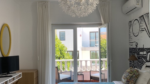 A hotel room with a bed, a desk with a computer, a TV, a balcony with chairs, and a view of the outside. - Manelisa Cascais (Cascais)