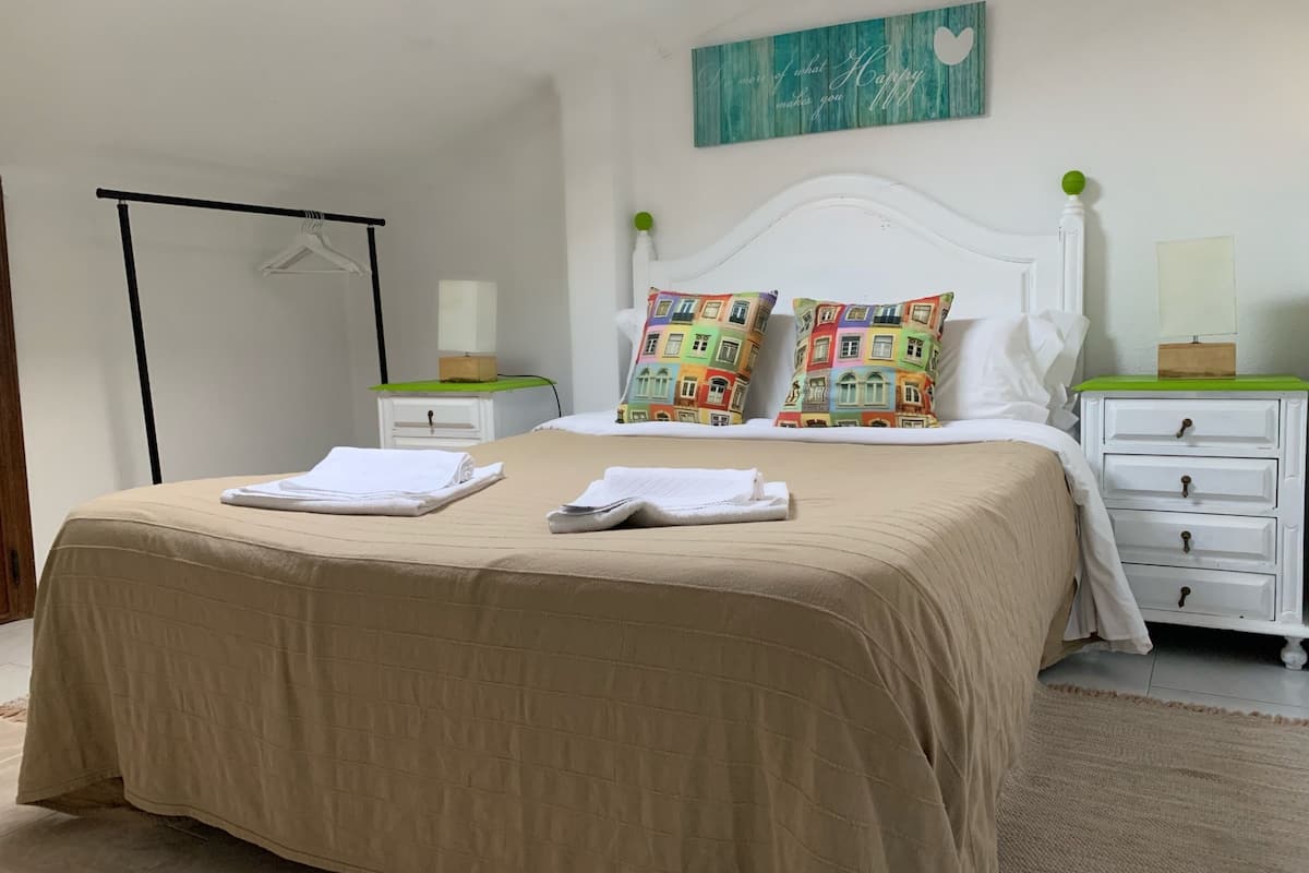Una cama bien hecha con dos almohadas, una mesita de noche con una lámpara y una obra de arte colgada en la pared.