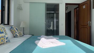 A hotel room with a bed, a bathroom with a glass door, and a wooden door.