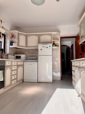 A kitchen with white cabinets, a microwave, a refrigerator, and a dishwasher. - Manelisa Cascais (Cascais)