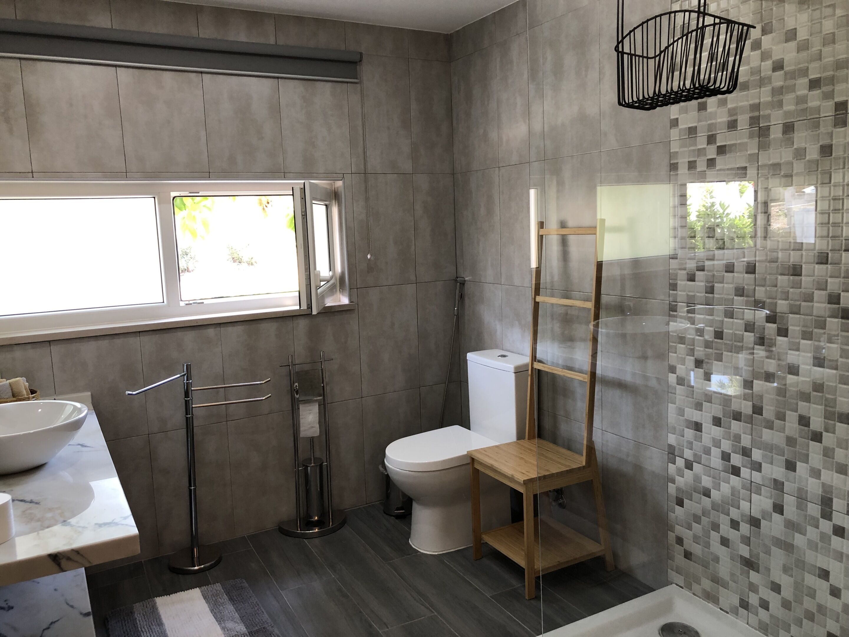 A modern bathroom with a large window, a sink, a toilet, and a shower area.