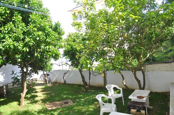 A backyard with a small table and chairs, a grill, and a white wall. - Manelisa Cascais (Cascais)