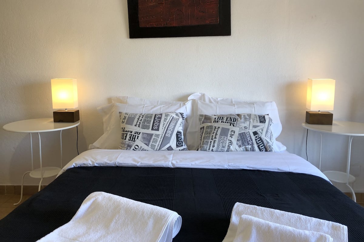 Una habitación de hotel con una cama bien hecha, dos mesitas de noche con lámparas y un cuadro en la pared.