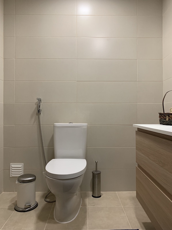 A modern bathroom with a toilet, bidet, and trash can.