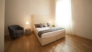 A bedroom with a bed, a chair, a bedside table with a lamp, and a window with curtains. - La Porta del Paradiso (Florence)