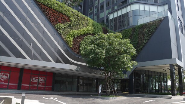 A modern building with a sloped roof, a tree in the center, and a red storefront with signage. - Sky Home at Bangkok-Bangna (Bangkok)