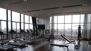A spacious gym with treadmills, elliptical machines, and weight benches. Large windows offer views of the cityscape. - Sky Home at Bangkok-Bangna (Bangkok)