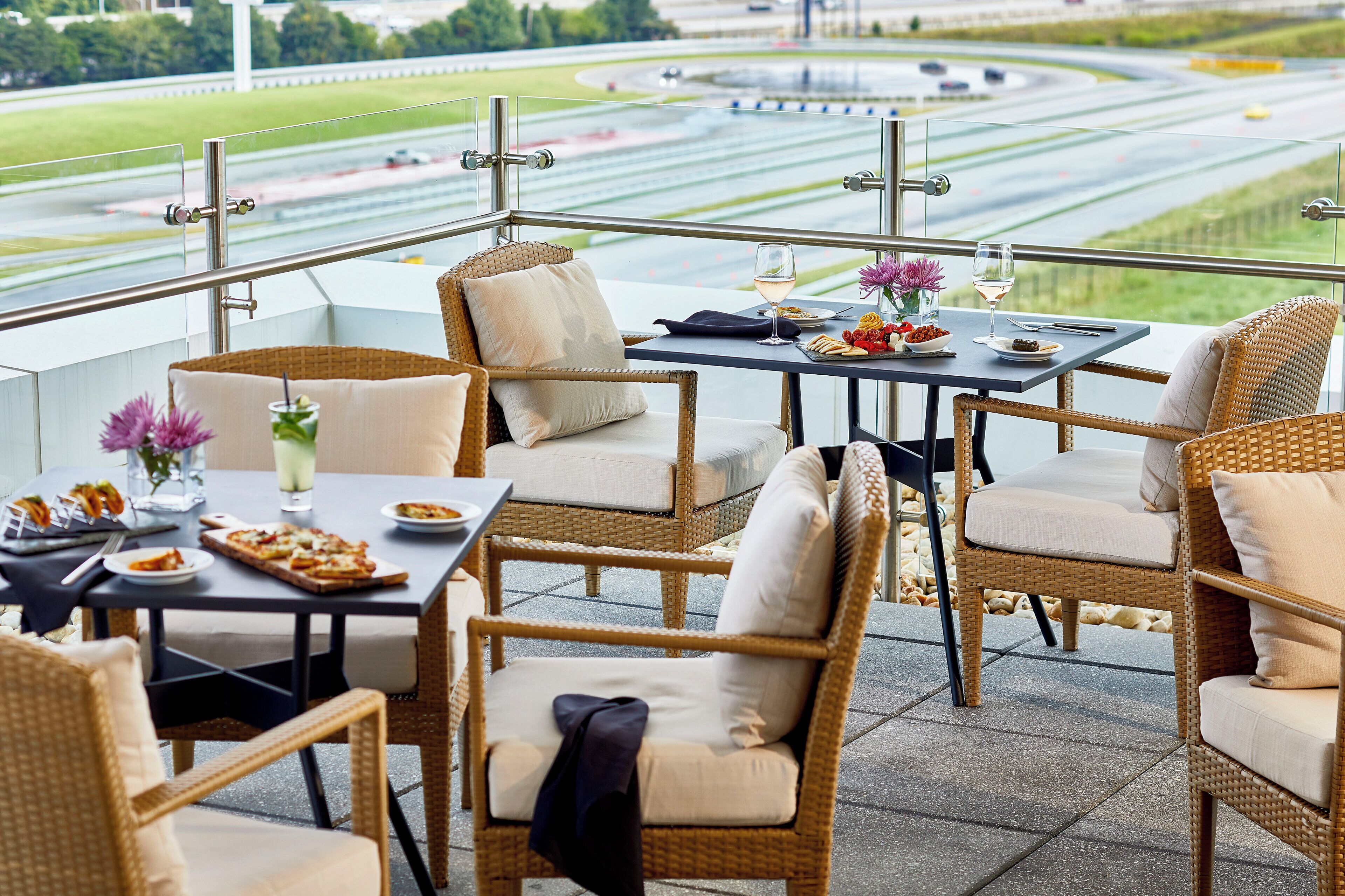 Une terrasse dotée de meubles en osier, de tables pour prendre les repas en plein air et offrant une vue sur un circuit de course.