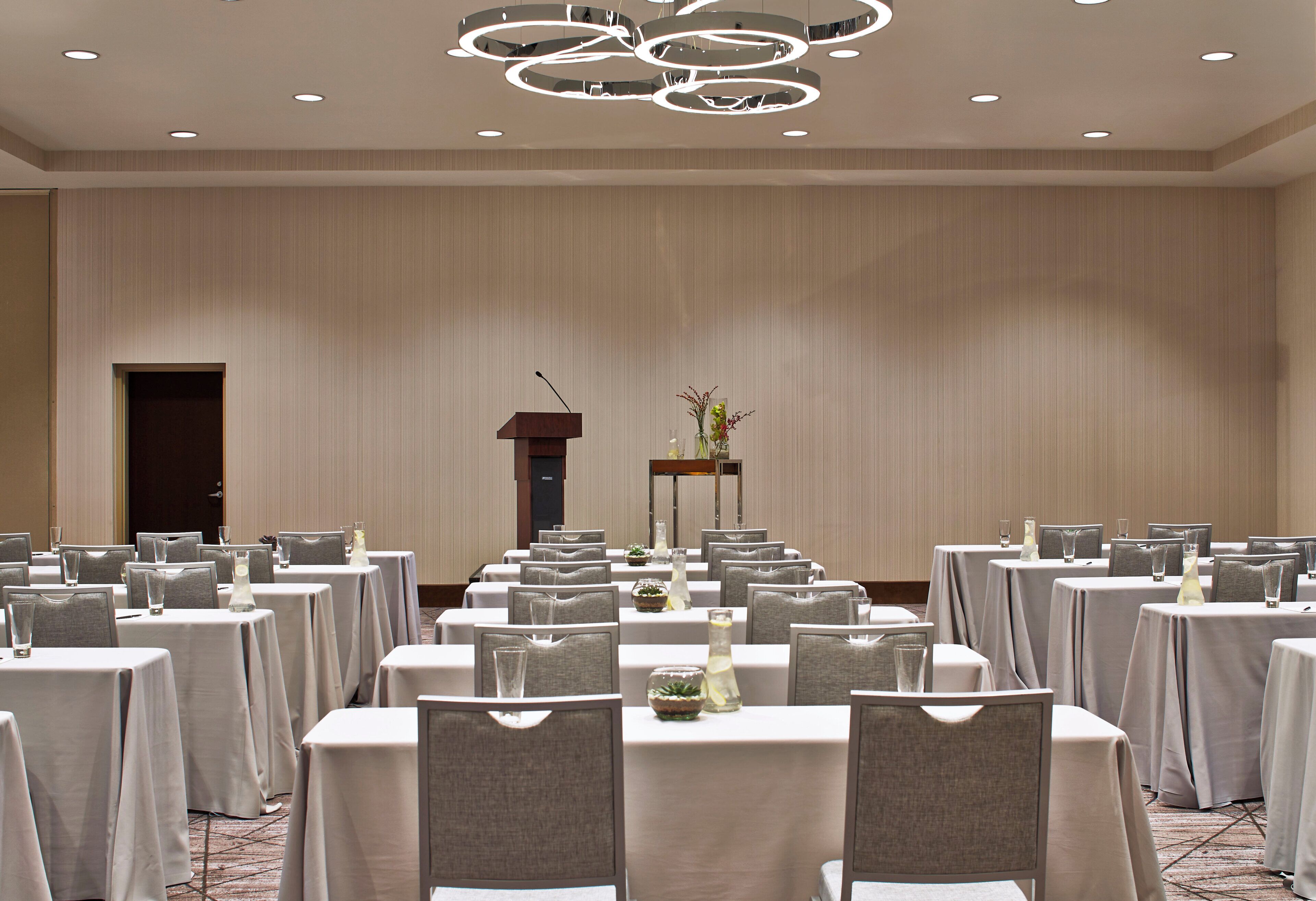 A conference room with tables set for a meeting, a podium, and a decorative vase with plants.