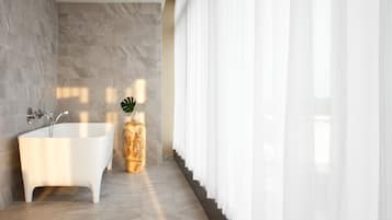 A modern bathroom with a freestanding bathtub, marble walls, and a potted plant.