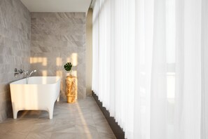 Un baño moderno con una bañera independiente, paredes de mármol y una planta en maceta.