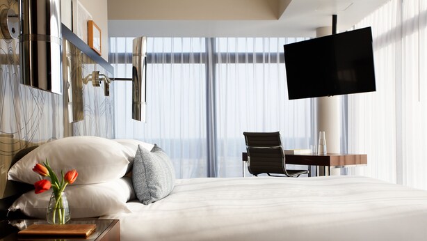 Ein Hotelzimmer mit einem großen Bett, einem Schreibtisch mit Stuhl, einem Flachbildfernseher und einer Tischlampe mit Blumen auf dem Nachttisch.