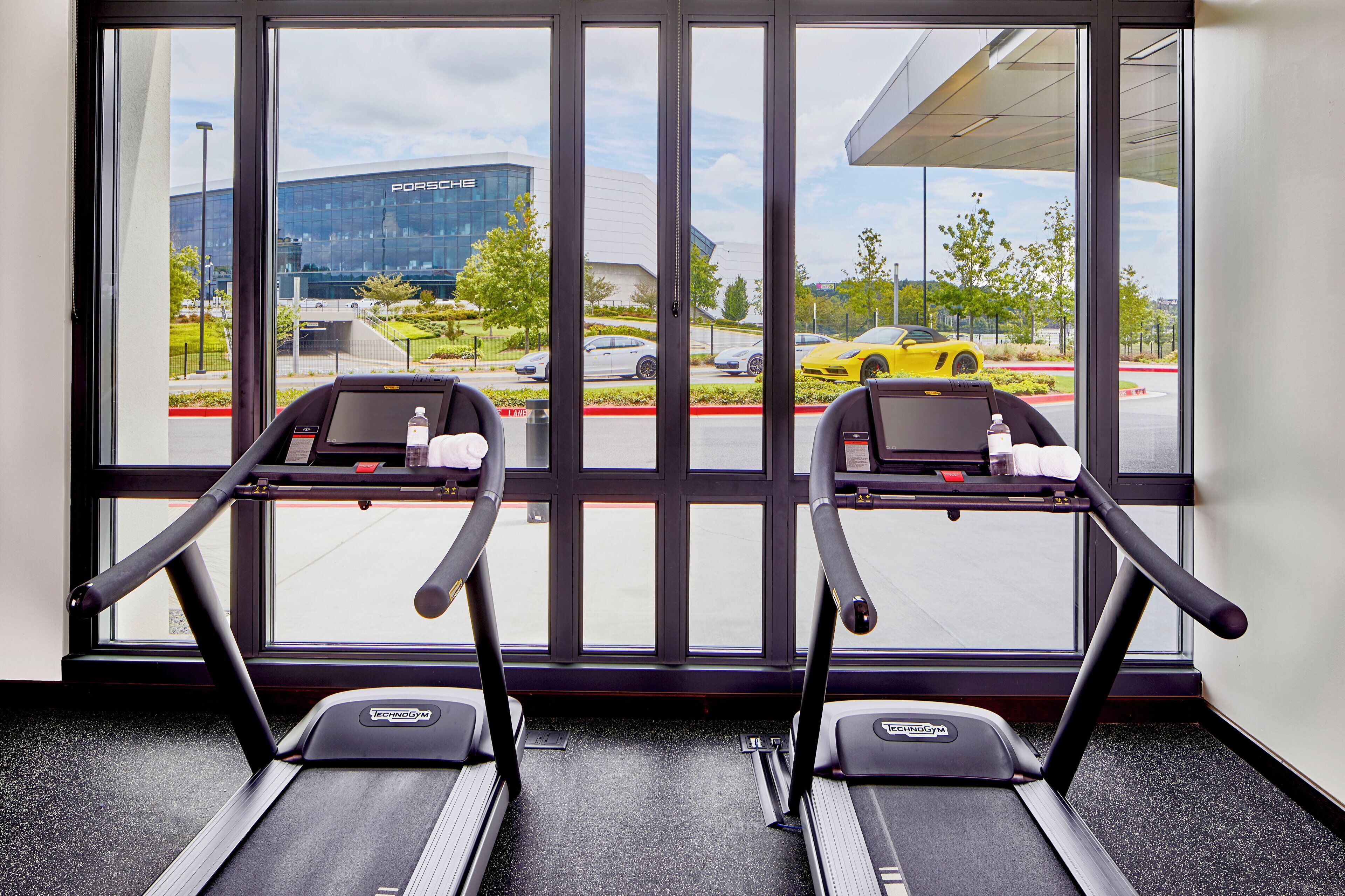 A gym with treadmills and a view of a parking lot with cars and a building in the background.
