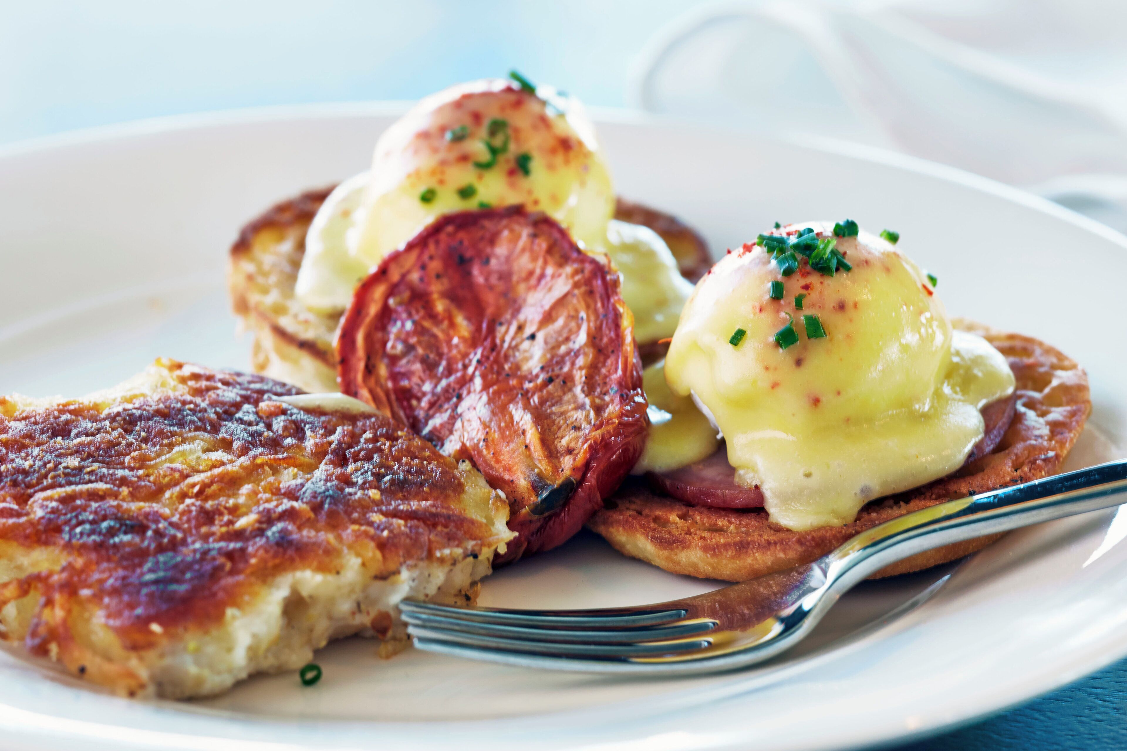 Une assiette avec des œufs Bénédicte, des pommes de terre rissolées et une tranche de pain grillé.