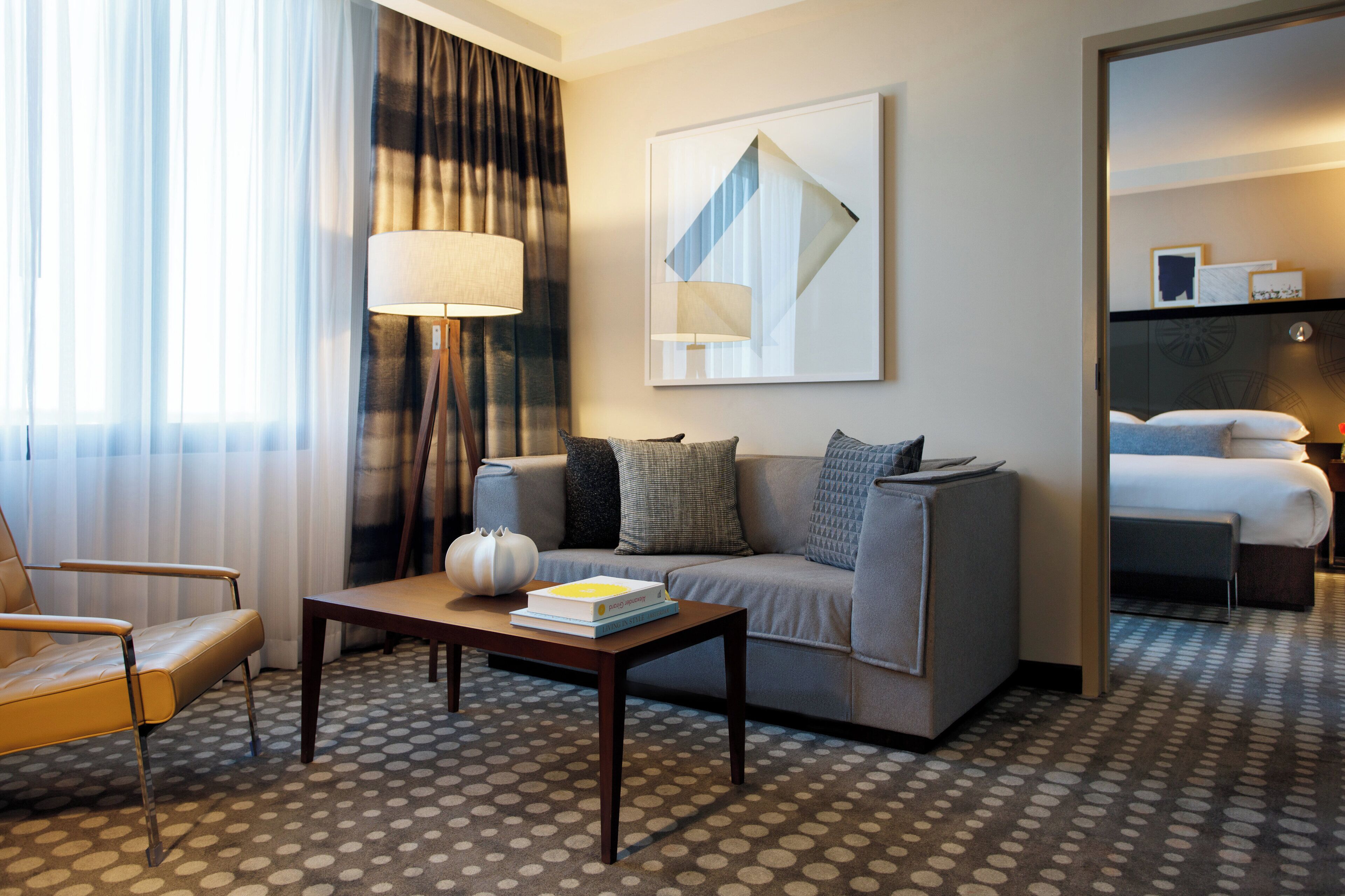 Ett hotellrum med en soffa, ett soffbord, en lampa, en säng och en tavla på väggen.
