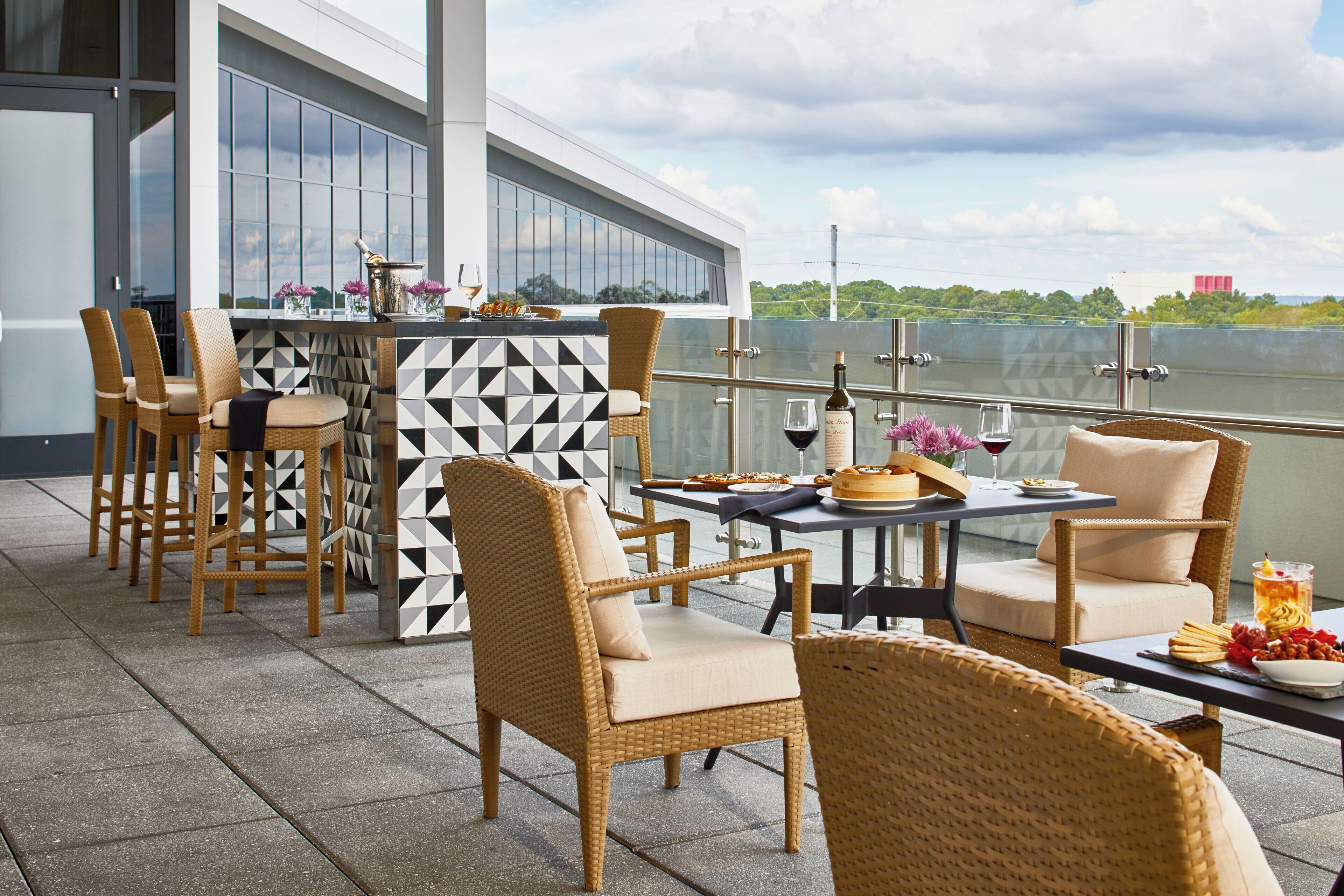 An outdoor dining area with wicker chairs and a table set with food and drinks, overlooking a body of water.