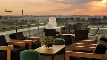 Una terraza en la azotea con mobiliario exterior, vistas al aeropuerto y un atardecer de fondo.
