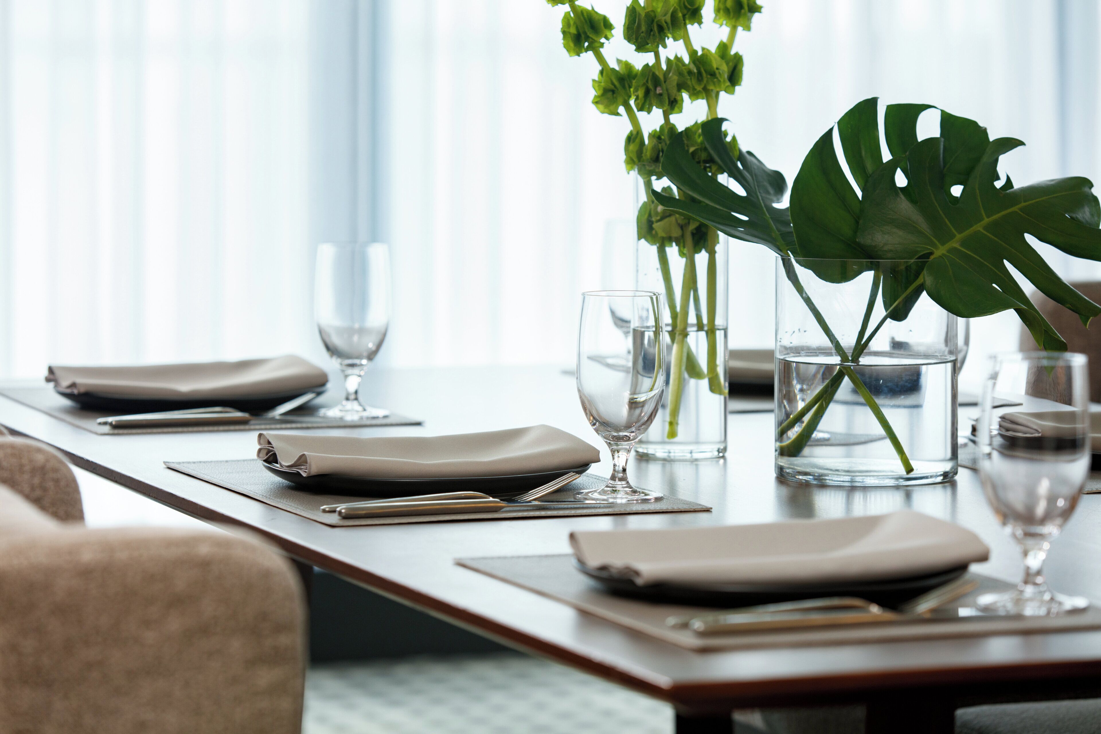 Une table à manger dressée avec des assiettes, des couverts et des verres, et un vase avec une plante.
