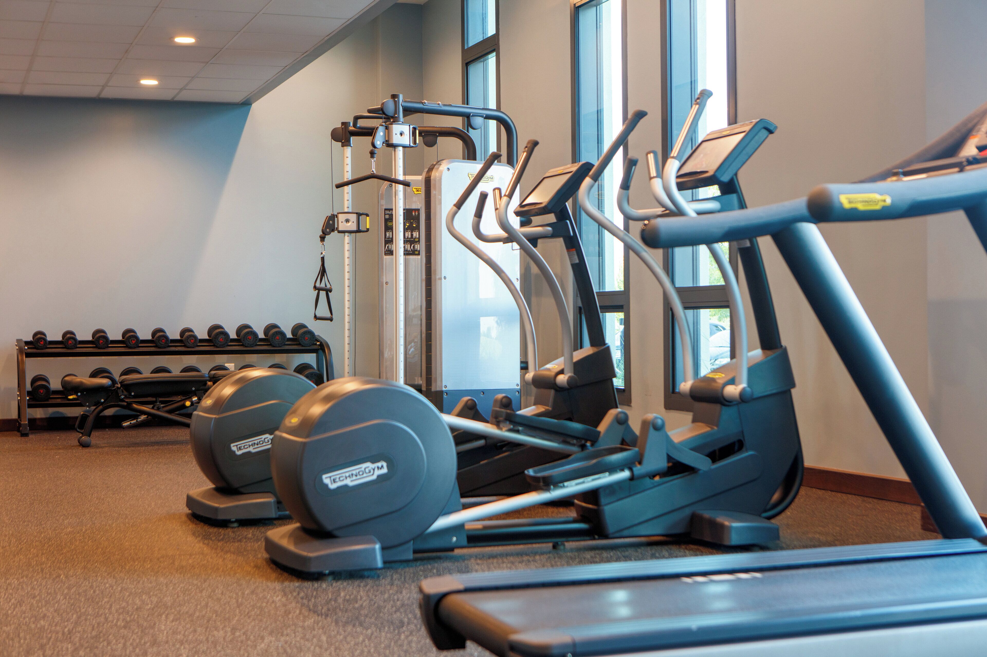 A gym with exercise equipment including treadmills, elliptical machines, and dumbbells.