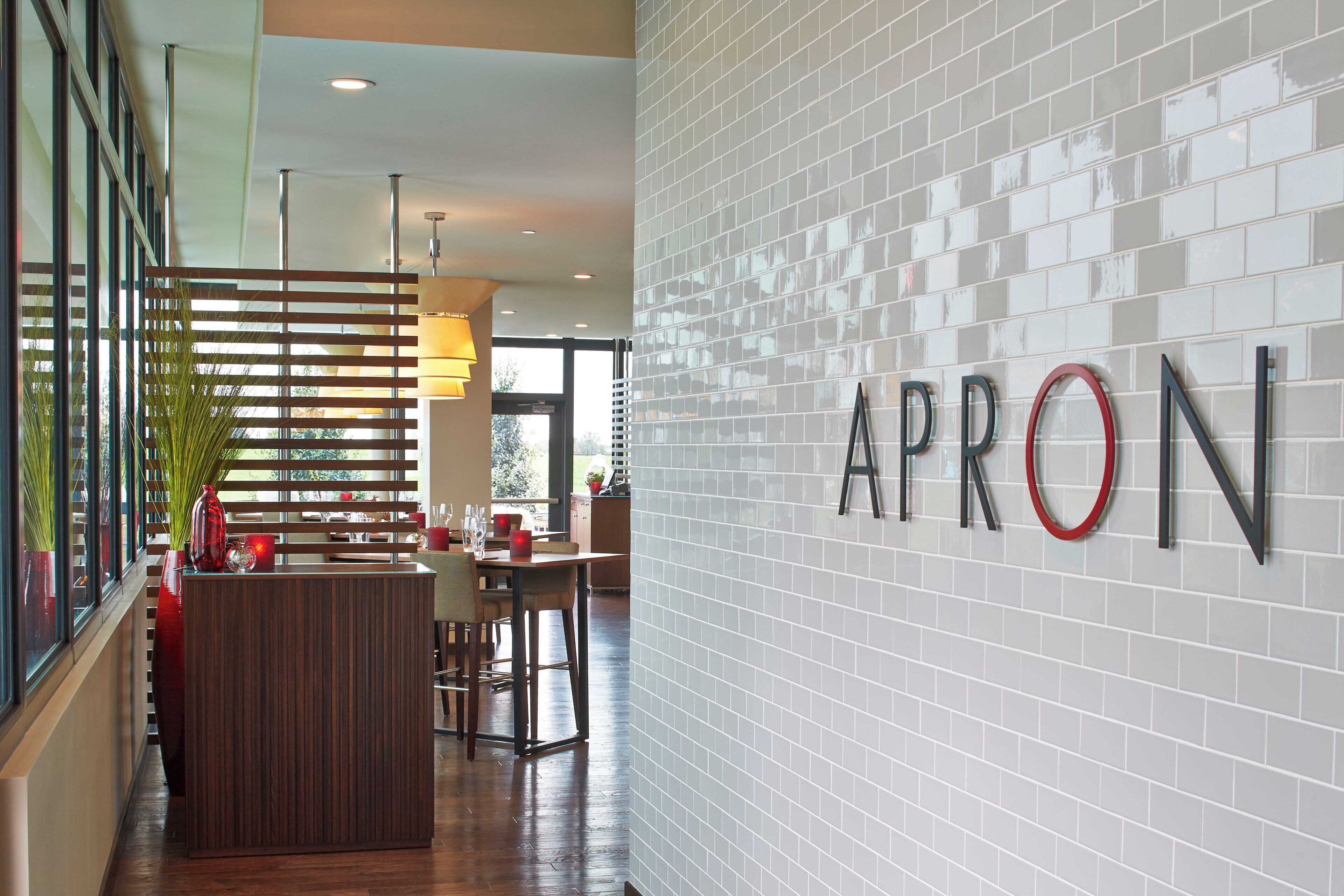 A modern interior with a reception desk, a dining area, and a wall with the word 'APRON' displayed.