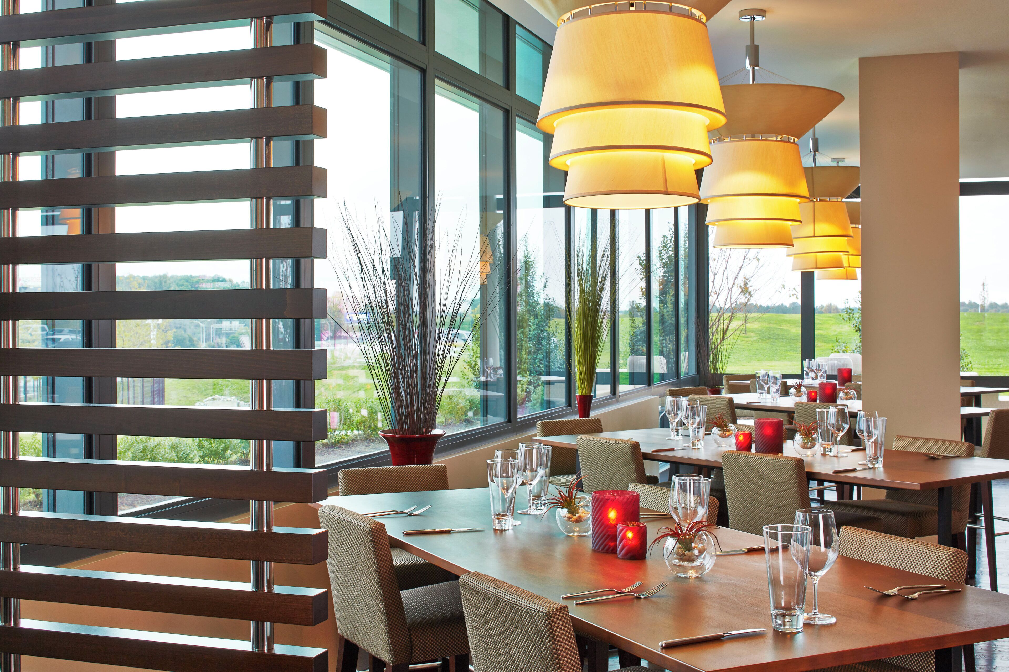 A restaurant with large windows, wooden slats, and multiple tables set for dining.