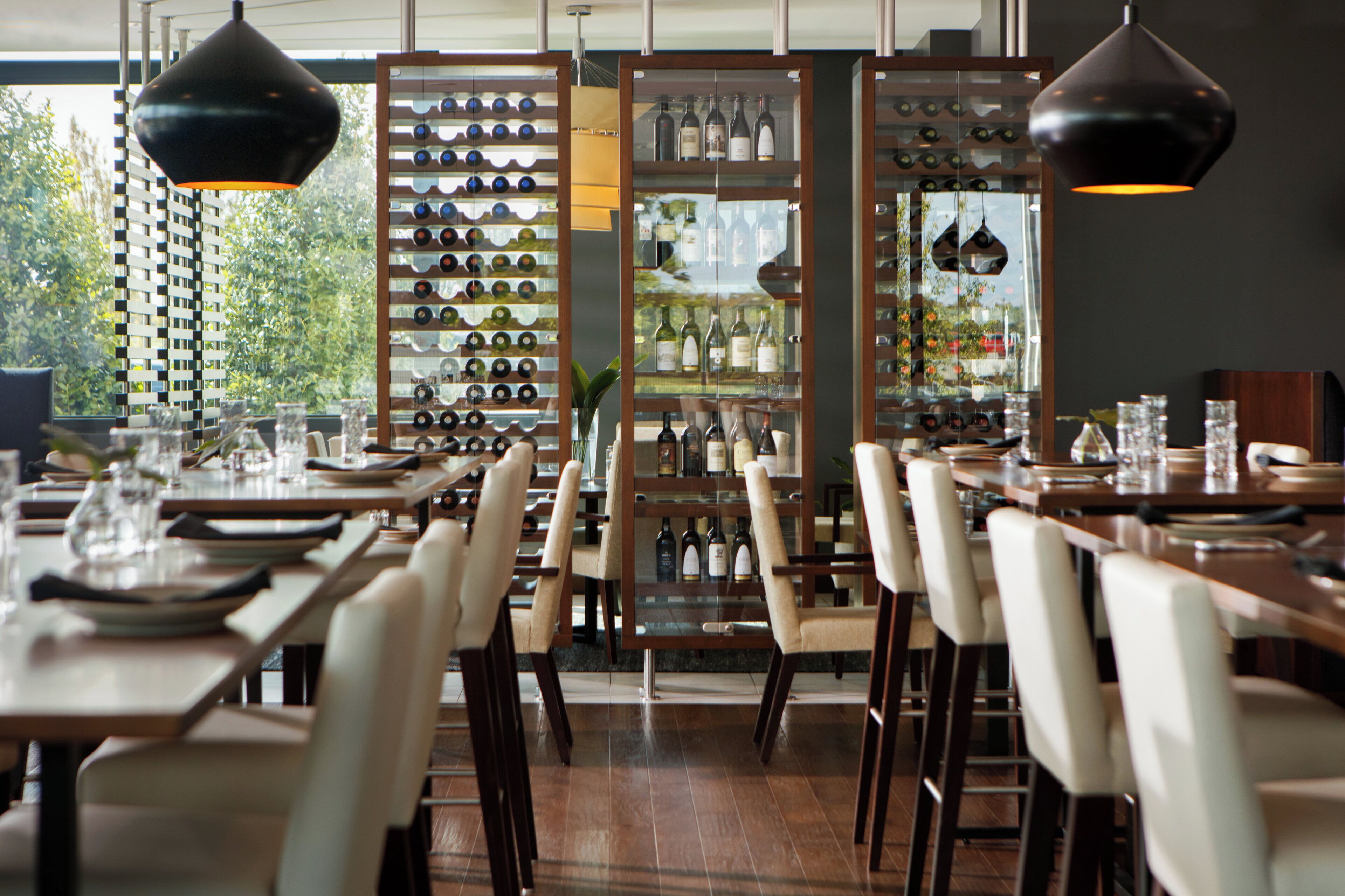 A restaurant interior with multiple dining tables, chairs, and a wine display.