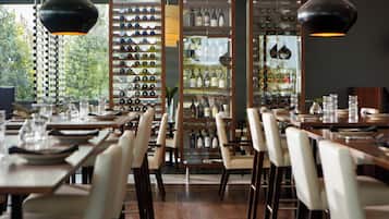 A restaurant interior with multiple dining tables, chairs, and a wine display.