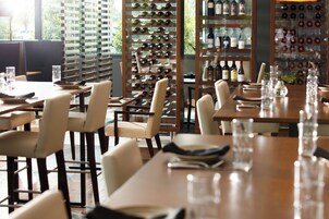 Interior de restaurante com várias mesas, cadeiras e estantes de vinhos cheias de garrafas.