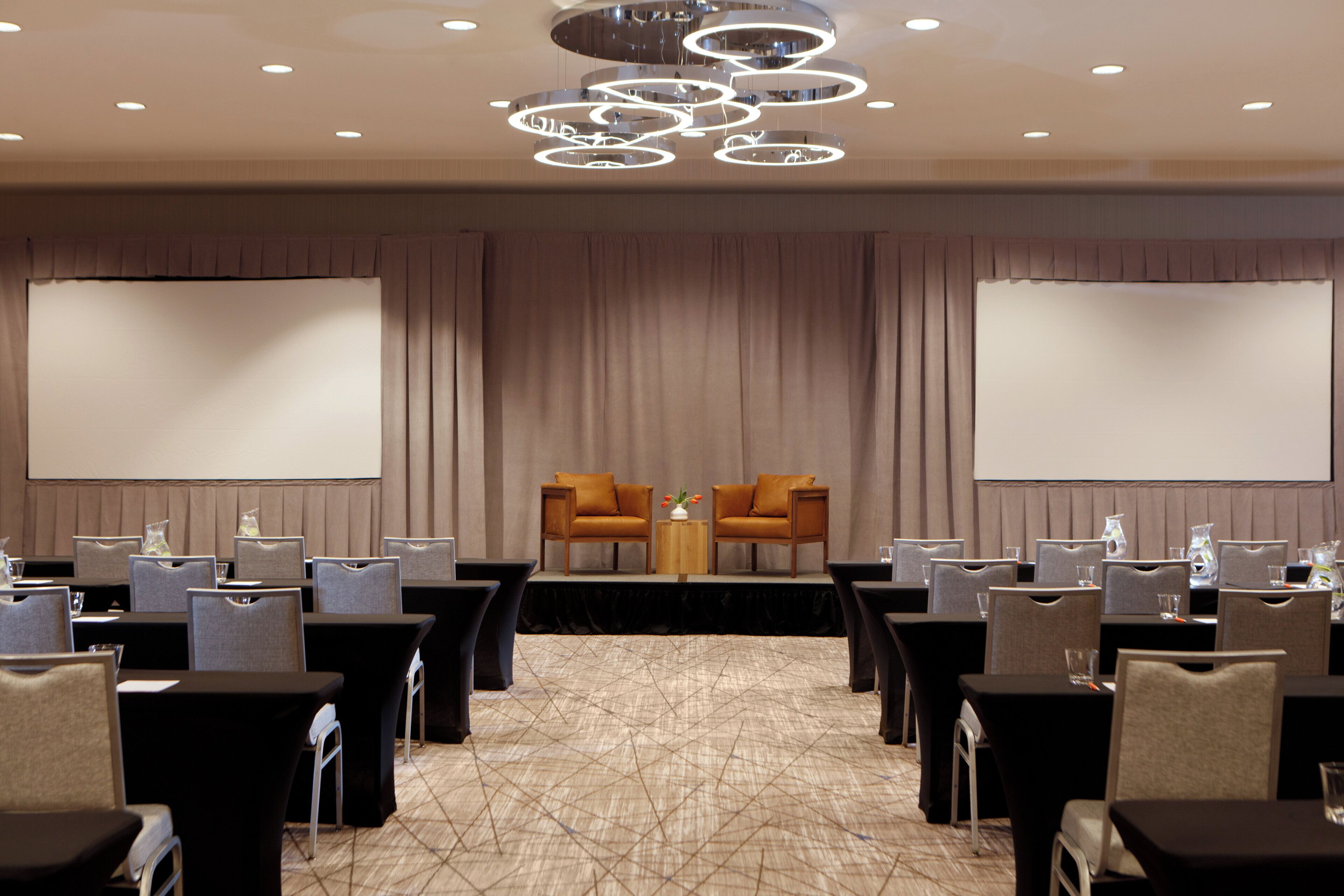 A conference room with a stage, two sofas, and rows of tables and chairs.