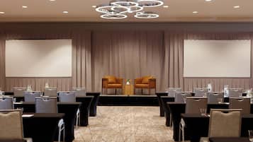Un salón de conferencias con un escenario, dos sofás y filas de mesas y sillas.