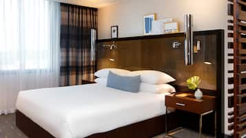 Ett hotellrum med en stor säng, ett nattduksbord med en vas och en spegel.