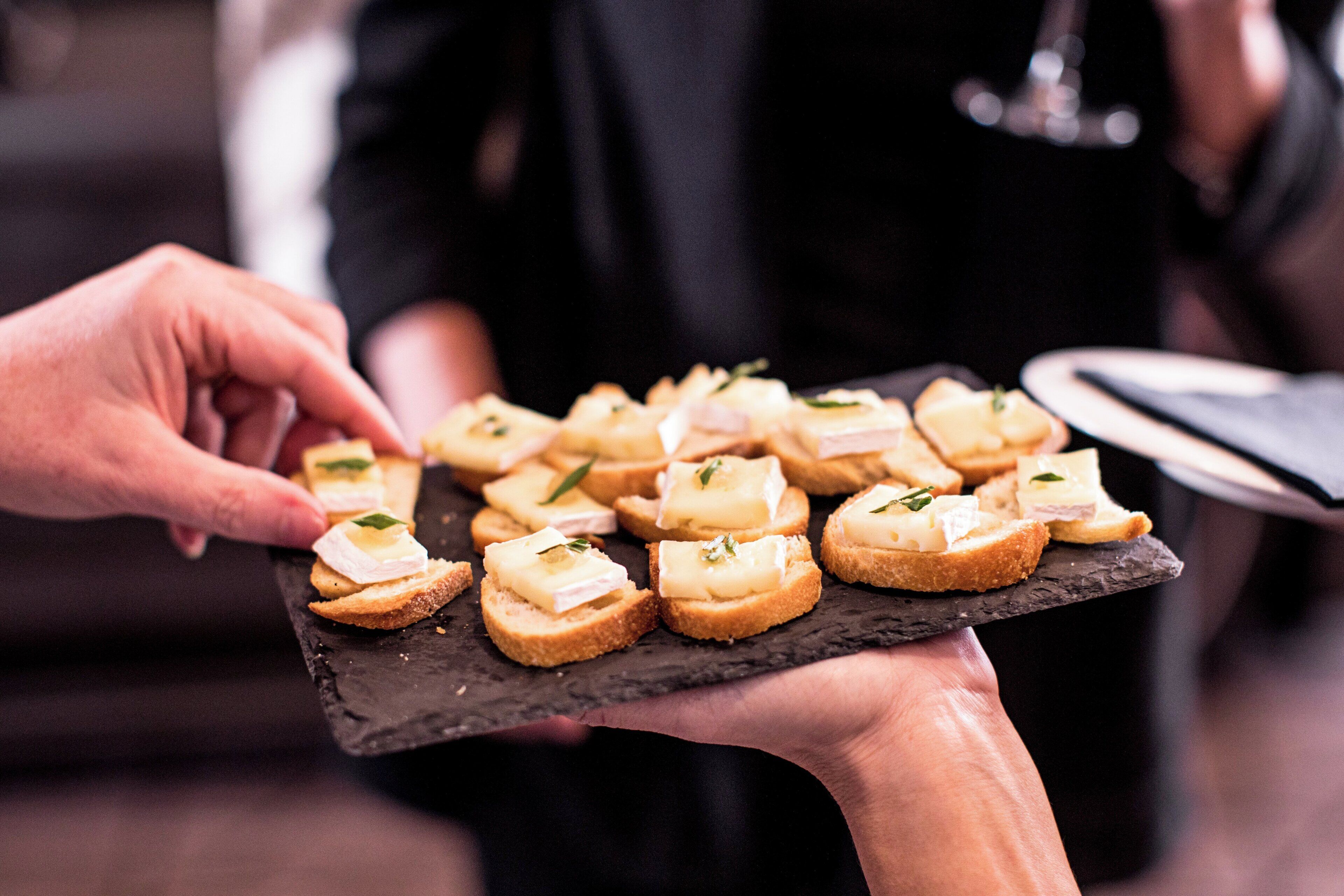 A person holding a slate board with small appetizers.
