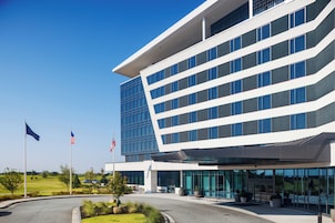 A modern building with a glass facade, a flat roof, and a landscaped entrance area.