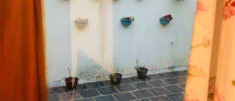 A courtyard with potted plants on a tiled floor, a white wall, and a wooden door.