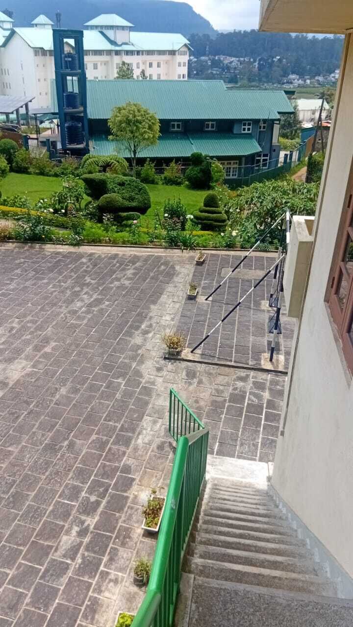 Vista desde un balcón sobre un patio con una escalera, barandilla verde y un edificio con techo verde al fondo.