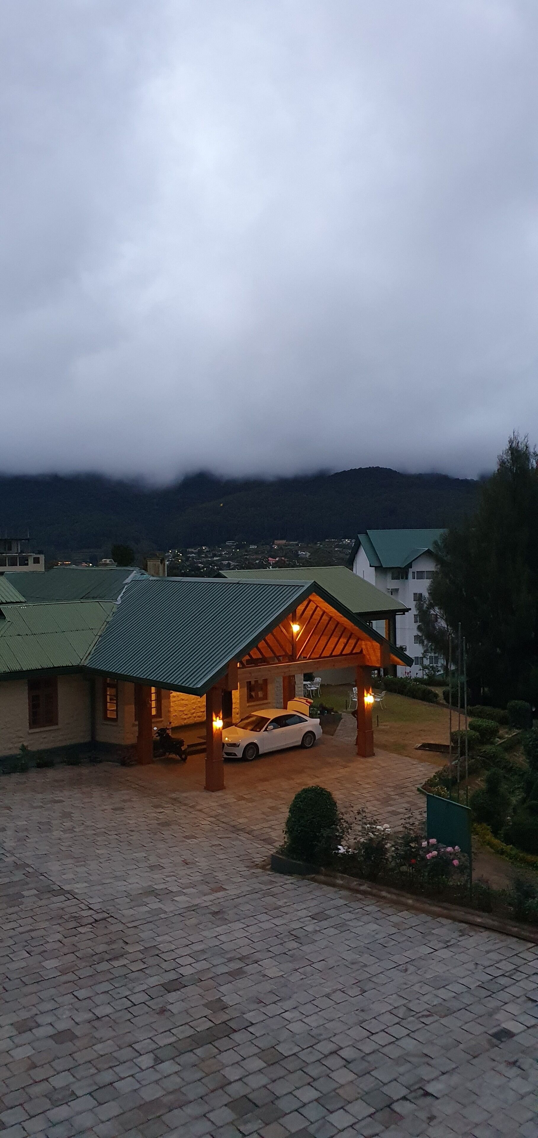 Un bâtiment doté d’un espace extérieur abrité, une voiture garée devant, et un paysage montagneux en arrière-plan.