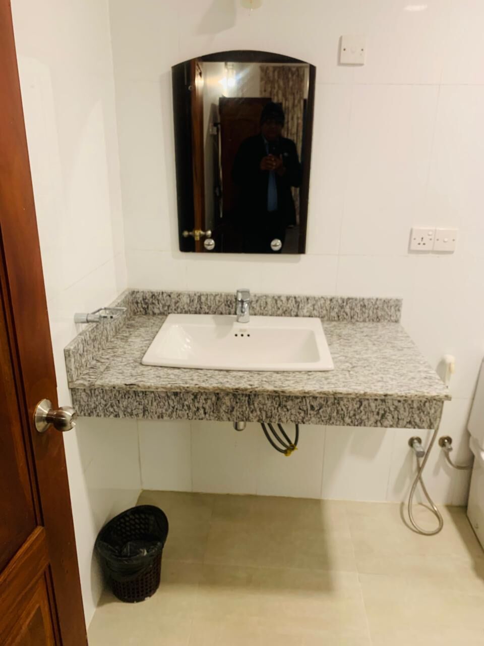 A bathroom with a granite countertop sink, a mirror above it, and a black trash bin.